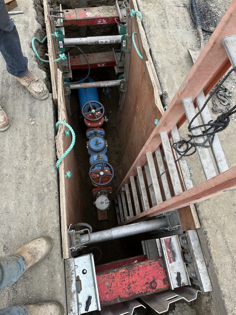 Blue PVC water main with gate valves installed in a shored trench